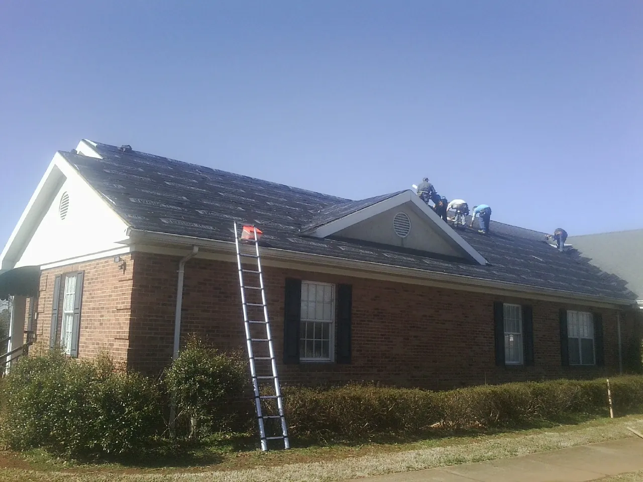 Crew tearing shingles off a brick ranch roof with a ladder set — Emergency Roof Repair work by our crew in Dowelltown