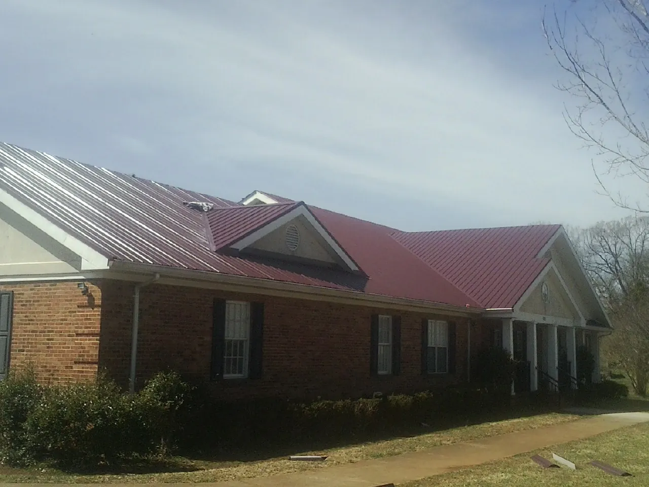 Red metal roof with gabled entries on a long brick building, from a Hail Damage Roof Repair job in Dowelltown