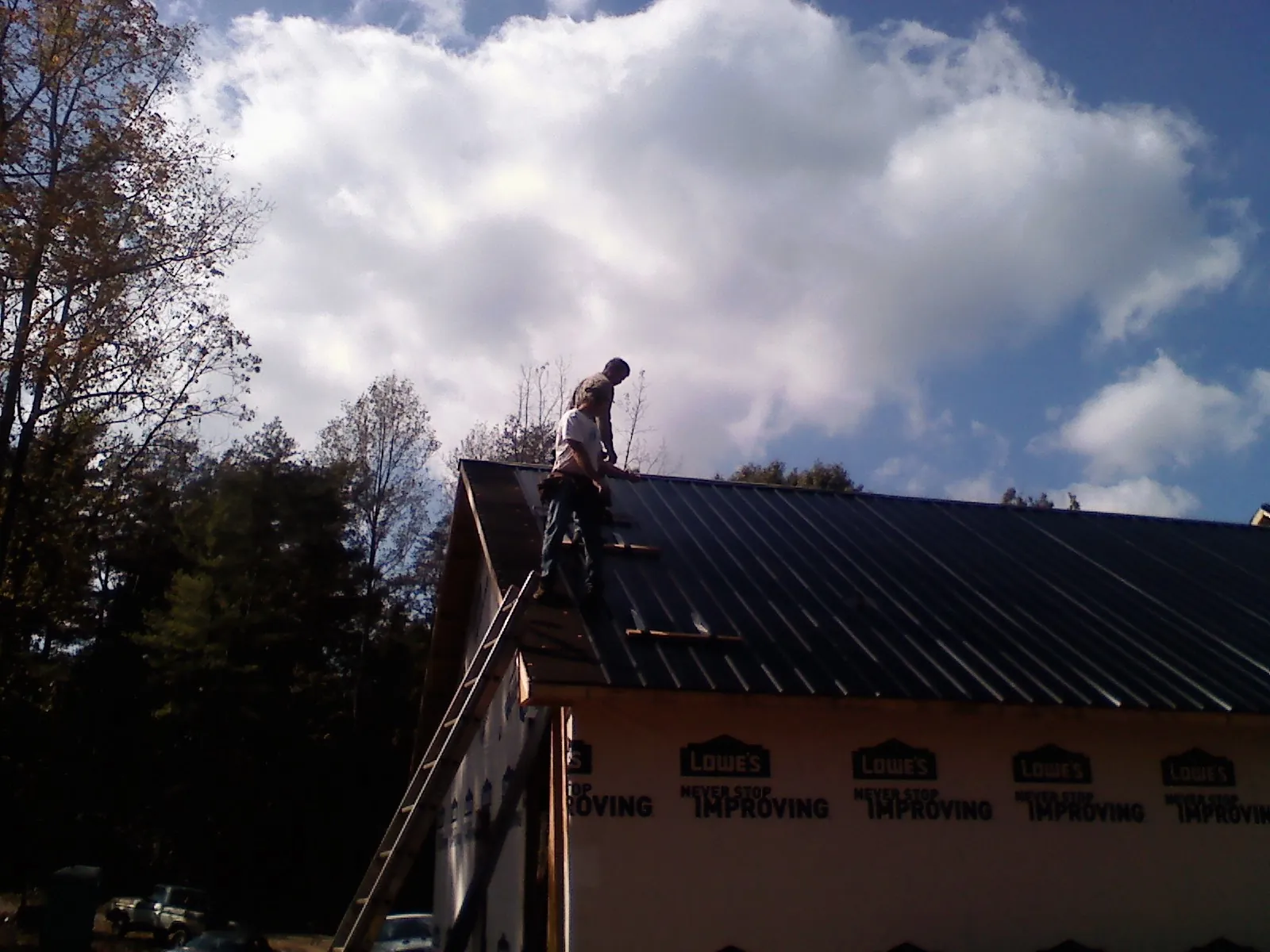 Roofer fastening dark metal panels high against a cloudy sky, from a Roof Inspection job in Dowelltown