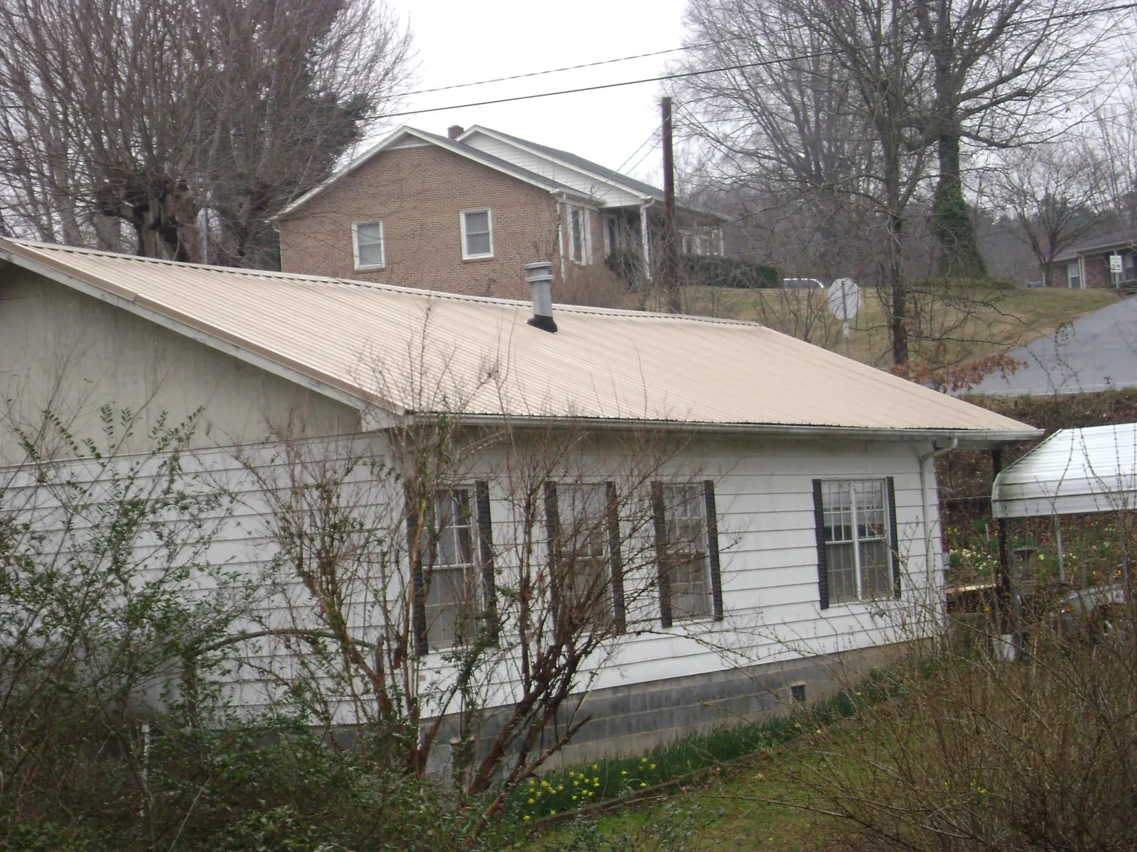 Tan metal roof on a white sided house set into a hillside — Commercial Roofing by Roofing Brothers in Dowelltown